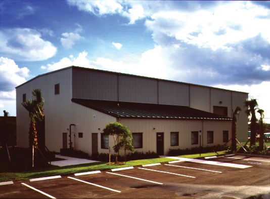 Single-story pre-engineered metal building with light-colored exterior panels and adjacent parking lot.